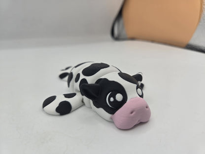 Sea Cow Manatee flexi 3D print in black and white cow-spot colors with a pink nose, front three-quarter view lying on a white surface