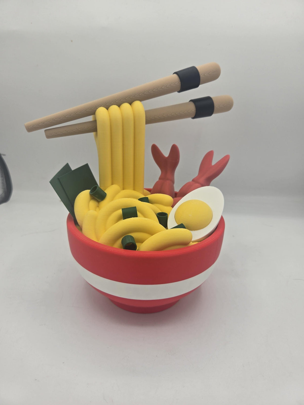 Ramen Bowl Display and Stash 3D print front view: red and white bowl piled with yellow noodles, two shrimp, a halved egg, seaweed and chopsticks lifting the noodles