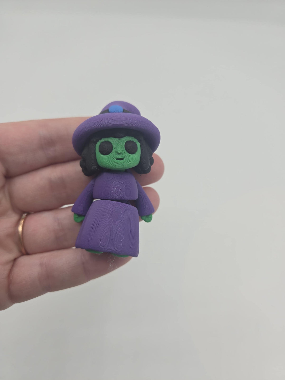 Tiny Witch Articulated Flexi Mini 3D print regular-nose cute style held in a hand for scale, purple hat and robe with green skin and black hair