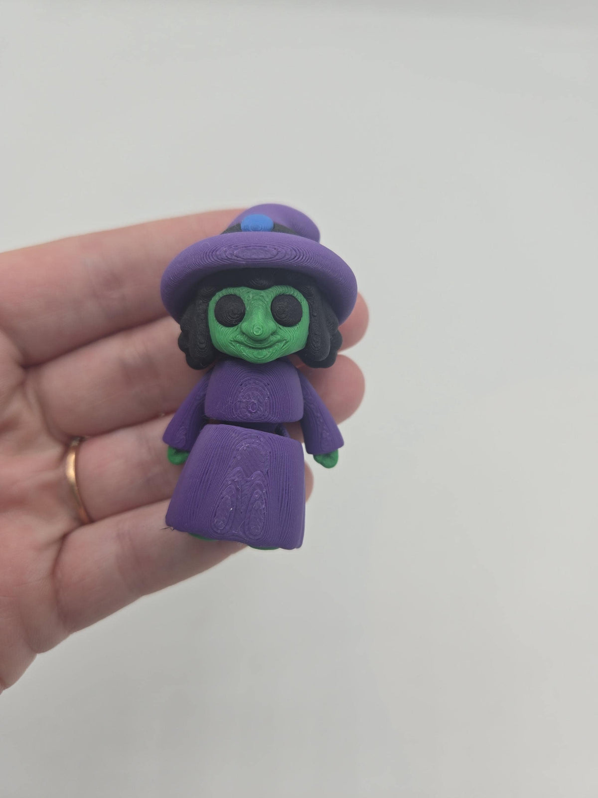 Tiny Witch Articulated Flexi Mini 3D print long-nose style held in a hand for scale, purple witch hat with blue band accent and green face