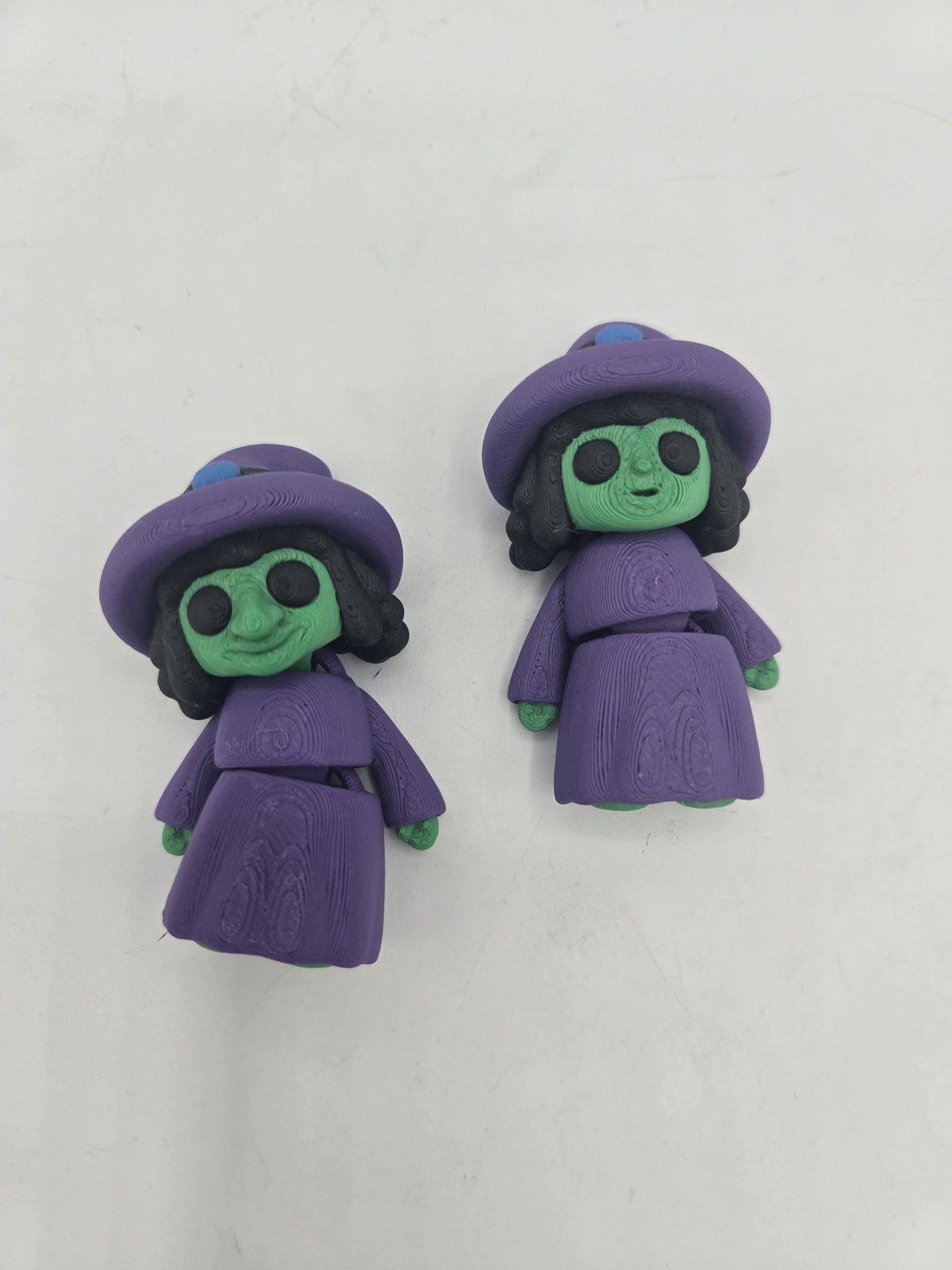 Tiny Witch Articulated Flexi Mini 3D print pair lying on a white surface, long-nose and regular-nose versions in purple robes with black curly hair