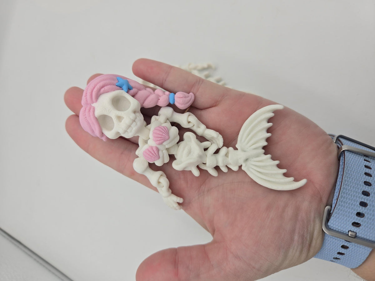 Flexi Mermaid Skeleton 3D print Hair + Clam Shells style held in an open palm to show its size, pink braid, blue starfish and articulated bony fin tail