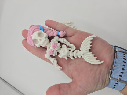 Flexi Mermaid Skeleton 3D print Hair + Clam Shells style held in an open palm to show its size, pink braid, blue starfish and articulated bony fin tail